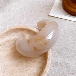 Detail shot of beige resin cuff bracelet with amber pattern on a minimalist stone tray