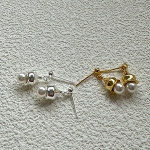 Close-up of minimalist gold and silver pearl stud earrings on a textured background