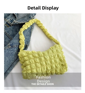 Close-up of light green bubble textured fabric handbag with ruched handle on white cloth