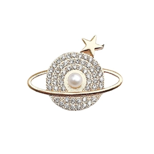 Golden Saturn brooch with center pearl and sparkling pavé crystals on white background