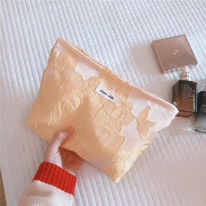Close-up of beige lace cosmetic bag with floral embroidery held in a lifestyle setting