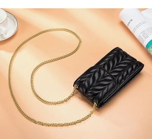 Detail of black quilted leather phone bag with elegant gold chain strap on warm background