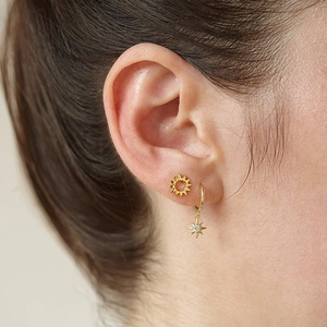 Detailed close-up of gold sunflower stud and star-shaped earring with zircon on ear