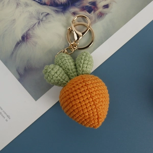 Handmade crochet carrot keychain with orange yarn and green leaves on a book background