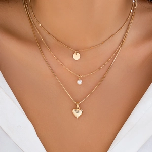 Close-up of three-layer gold necklace featuring disk, pearl, and heart pendants on model