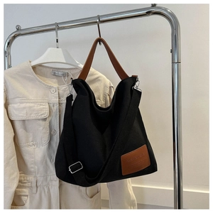 Detail of black canvas tote bag with brown leather handles and fashion logo patch