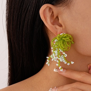 Handmade green and cream beaded bow earrings with tassel fringe on a model closeup