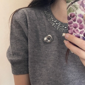 Minimalistische silberne Brosche mit fließendem Design auf grauem Strickpullover