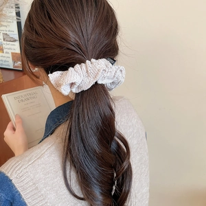 Detailed close-up of beige knitted scrunchie with fashion label on hair ponytail