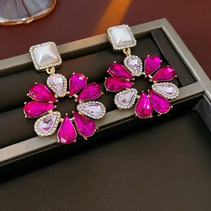 Dettaglio di orecchini a goccia dorati con cristalli rosa e madreperla quadrata