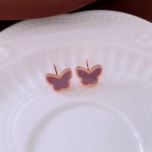 Detail of rose gold butterfly earrings with purple zircon on a white ceramic plate