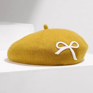 Détail d'un béret tricoté jaune gingembre avec un nœud blanc décoratif sur support blanc