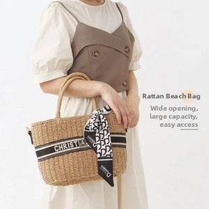 Detail of hand-woven straw beach bag with black handles and decorative logo silk scarf