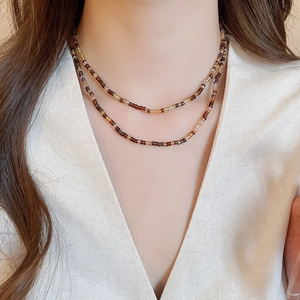 Detail of a double-layered necklace with brown and beige beads on a model neckline