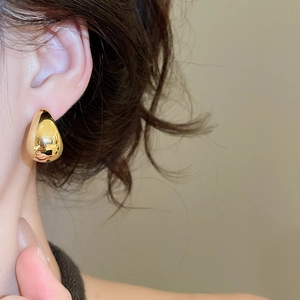 Close-up of a polished golden teardrop stud earring worn on the earlobe
