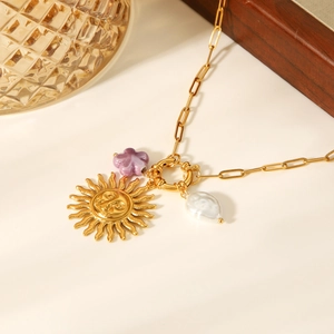 Nahaufnahme des goldenen Sonnenanhängers mit lila Blumenperle und weißer Barockperle