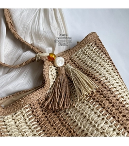 Close-up of vertical striped straw bag with dual tassels and decorative amber beads