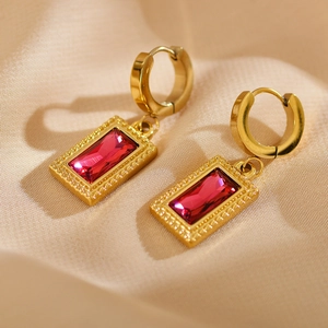 Macro shot of gold rectangle earrings with vibrant magenta zircon on soft beige fabric