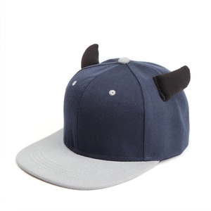 Detail of navy flat brim hat featuring decorative 3D devil horns and grey eyelets