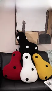 Detailed view of pear-shaped polka dot plush cushions in four colors on a leather sofa