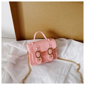 Detail of pink PVC jelly bag with gold metal chain strap on textured fabric