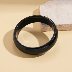 Close-up of polished black resin bangle with glossy finish on natural stone background