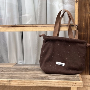 Close-up of brown wool felt drawstring bag with white polka dots on a wooden shelf