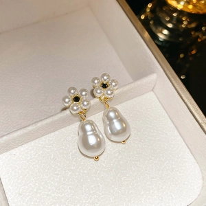 Detailed close-up of pearl flower earrings with gold plating on a textured jewelry box