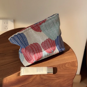 Detailed view of pumpkin jacquard fabric makeup bag on wood stool with soft shadows
