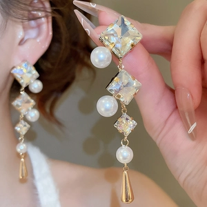 Detail of drop earrings with square crystals, white pearls, and golden cone pendants