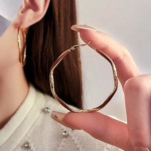 Close-up of model wearing oversized irregular geometric gold hoop earrings with a metallic finish