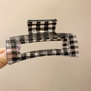 Detail view of a square acrylic hair claw clip featuring classic black and white grid patterns