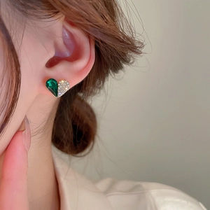 Close-up of emerald crystal heart stud earring with gold border worn by a model