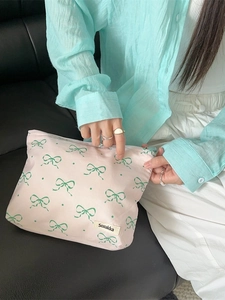 Floral makeup bag with green bow patterns and zipper, held by a model on a sofa
