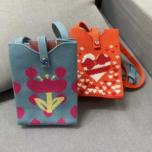 Detail of knitted shoulder bags in blue floral and orange heart pixel patterns