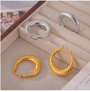 Detailed shot of twisted gold and silver hoop earrings on a beige velvet jewelry tray