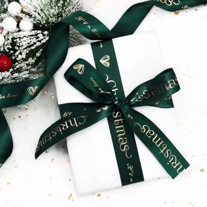 Dark green satin Christmas ribbon with gold lettering tied in a bow on white gift box