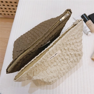 Détail des trousses à maquillage à texture gaufrée avec fermeture éclair en vert et crème