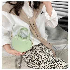 Detail of a mini light green heart-shaped jelly bag with gold chain strap on a model