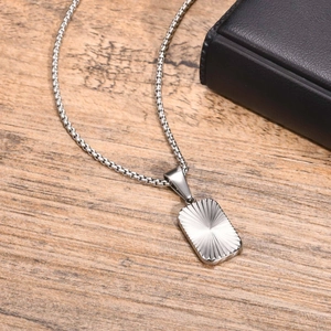Macro detail of silver rectangle pendant with sunburst texture on wooden background