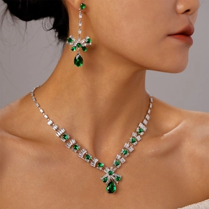 Detailed view of silver necklace and earrings set with green teardrop gemstones on a model