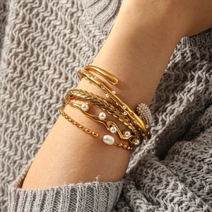 Primo piano di bracciali a strati placcati oro 18k con perle su uno sfondo di maglia grigia