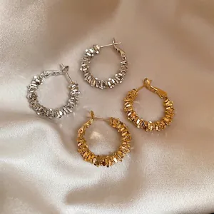 Irregular textured hoop earrings in gold and silver finish on elegant beige silk background