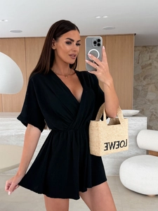 Dettaglio di una tuta estiva nera con scollo a V e una borsa tote in paglia intrecciata