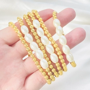 Dettaglio del set di bracciali elastici multistrato con perle dorate e perle finte bianche