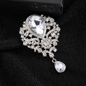 Macro view of crystal brooch with teardrop pendant and intricate silver scrollwork