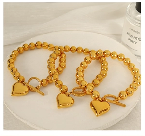 Detailed view of three golden bead bracelets with heart pendants on a white display tray