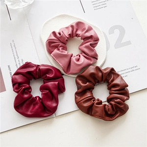 Detailed view of three PU leather scrunchies in pink, dark red, and brown colors