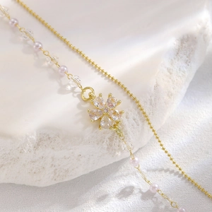 Dettaglio di bracciale a doppio strato con perline d'oro, perle rosa e ciondolo a fiore