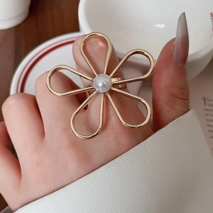 Makro-Detail eines großen goldenen Blumenrings mit Perle an einem Finger getragen